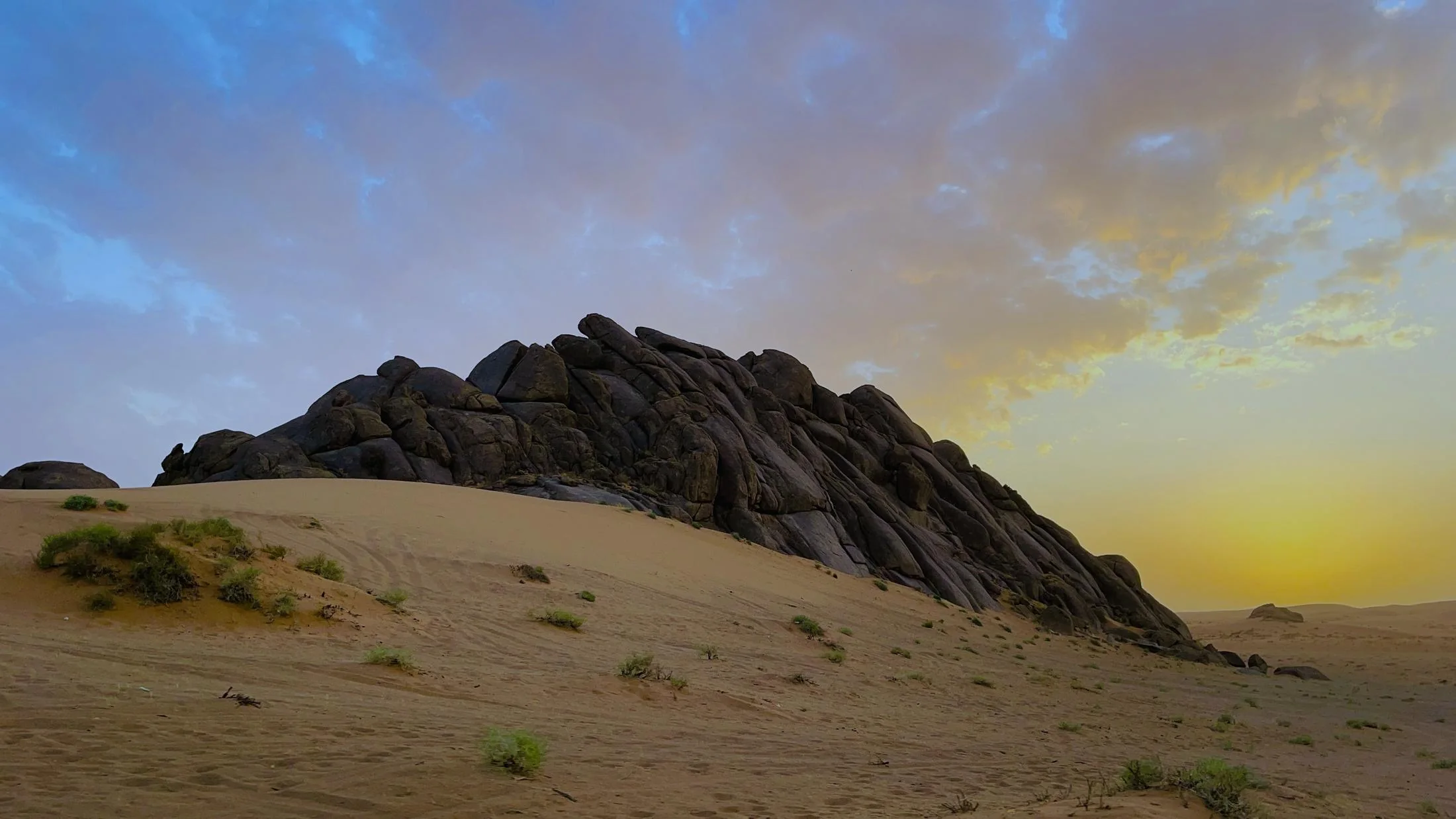 A rock outcrop rising out of desert sand in Saudi Arabia at first light